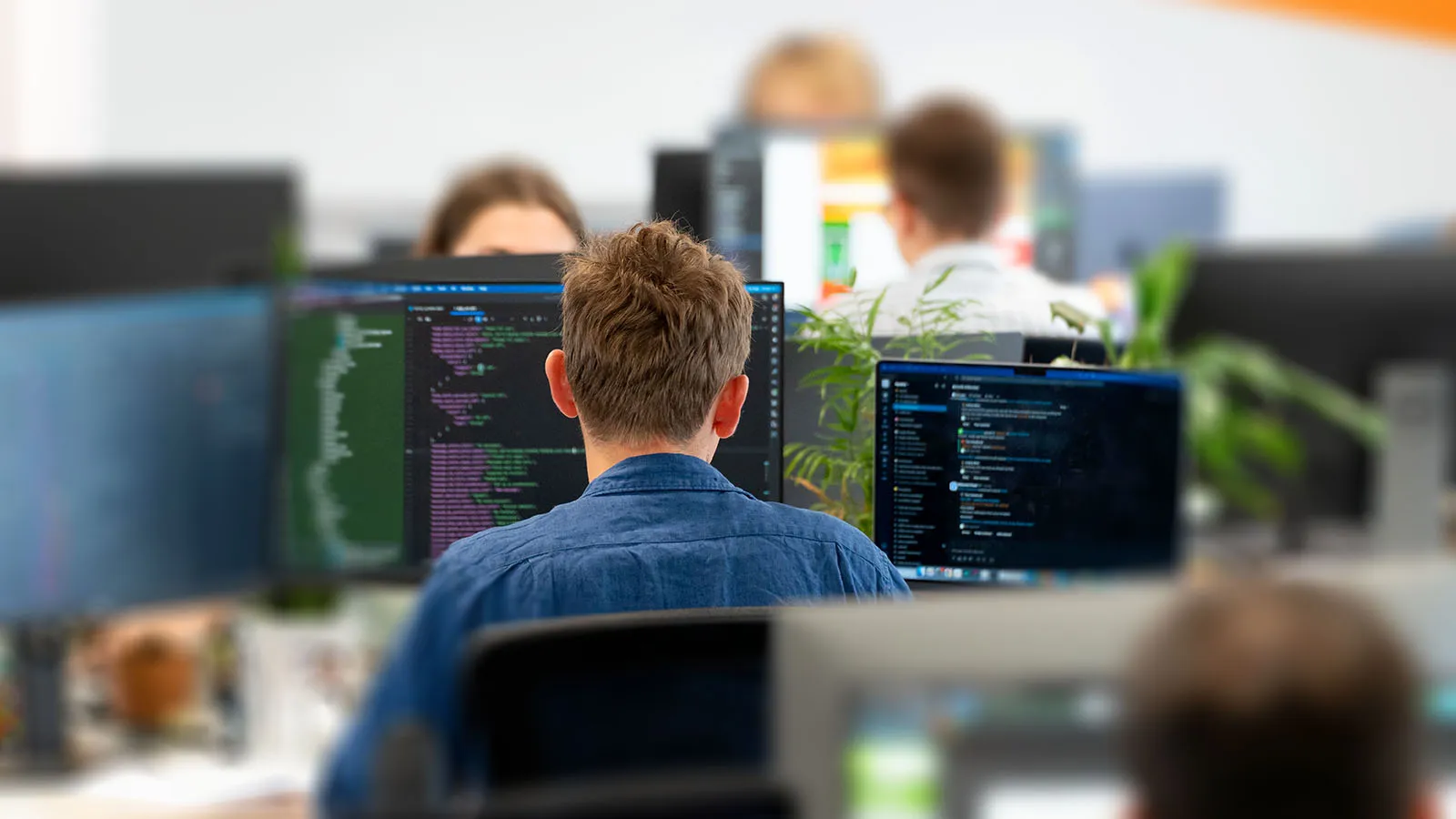 An over shoulder shot of a man sitting in front of screens displaying code.