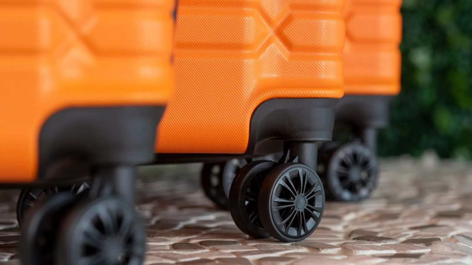 A close up of black wheels on three orange suitcases.