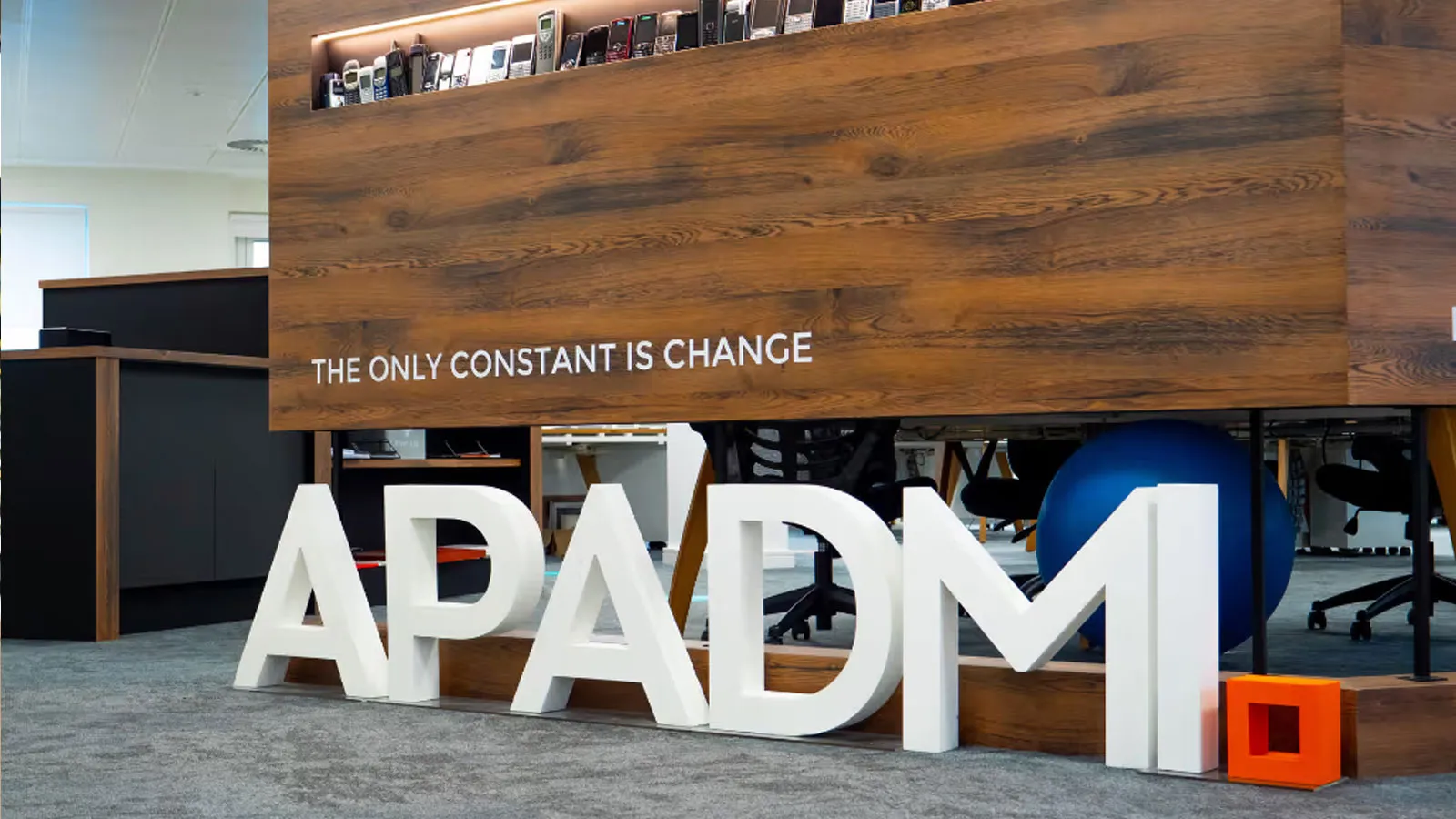 Big white letters spelling Apadmi, underneath a sign that says "the only constant is change"