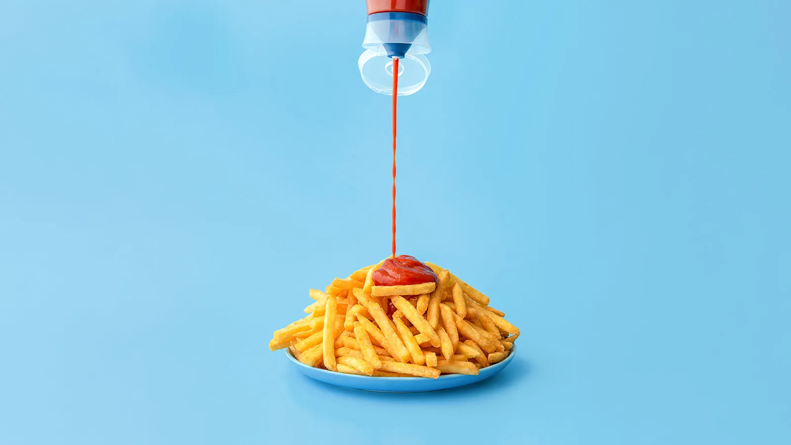 A plat of fries being squirted with ketchup.