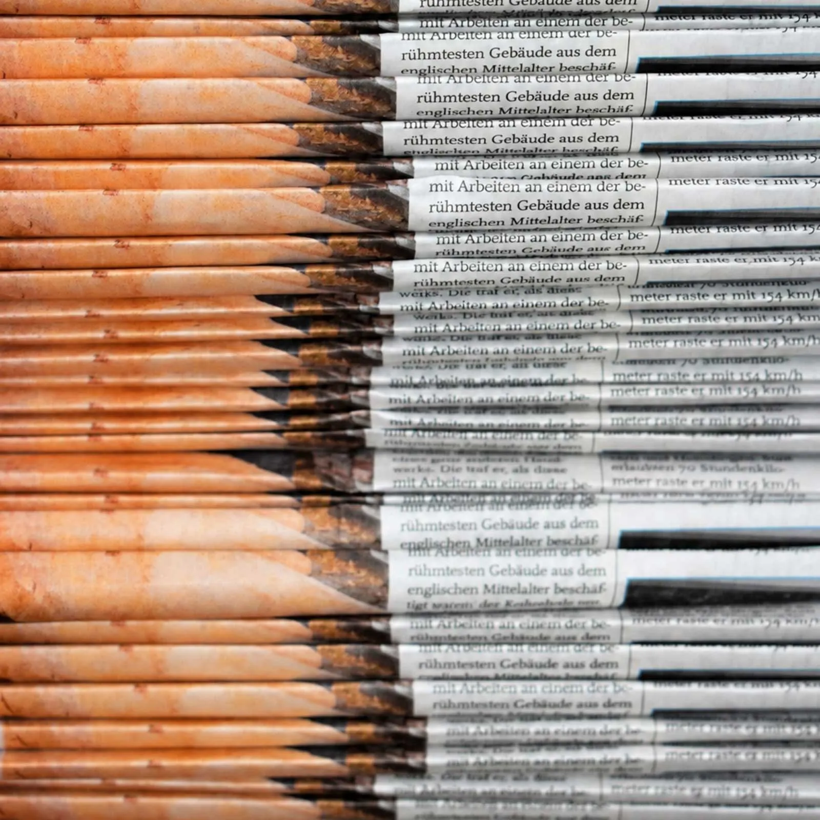 Close-up of a stack of folded newspapers, with warm orange tones on the left and printed news text on the right.